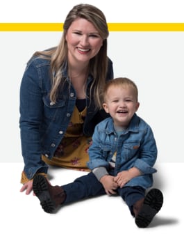 Snapshot of Emili, an advocate for Rebinyn® [Rebinyn Coagulation Factor IX (Recombinant), GlycoPEGylated ] kneeling next to her son Xander, who has mild hemophilia B. They are smiling and happy.